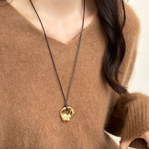 Gold irregular geometric pendant necklace on a brown cord worn by a model