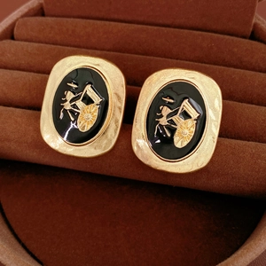 Macro shot of vintage gold earrings with black enamel and embossed carriage details