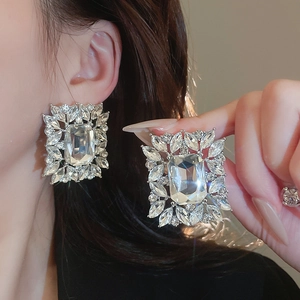 Close-up of luxury silver-tone statement earrings with large square zircons and leaf crystals