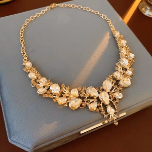 Close-up of sparkling gold droplet necklace with clear crystals on blue velvet