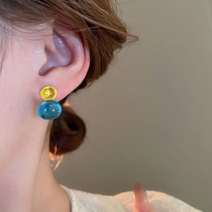 Detail of translucent dopamine gourd stud earrings featuring yellow and teal resin beads