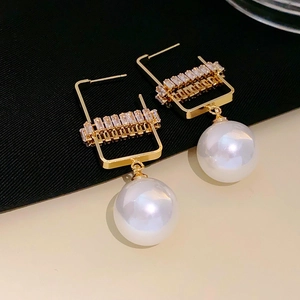 Detail view of geometric golden earrings with crystal accents and large white pearls