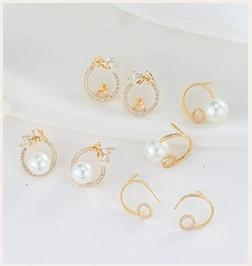 Detailed set of golden pearl earrings with leaf motifs and zircon stones on white fabric