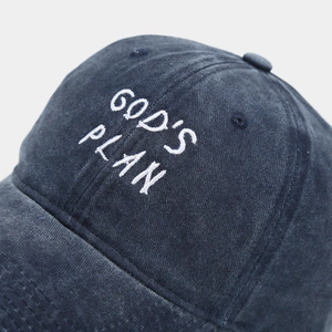 Detailed close-up of white GOD'S PLAN embroidery on washed charcoal cotton baseball cap