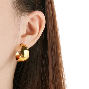 Close-up of golden wide C-shaped earrings with a polished mirror finish on model