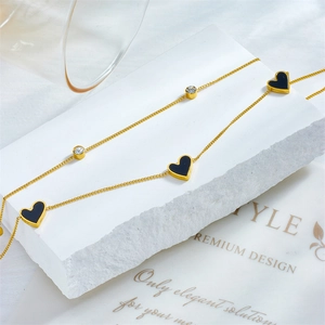 Golden chain anklet with black heart charms and small diamonds on a white stone background