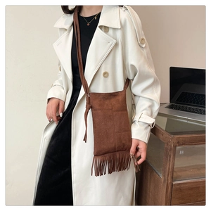 Brown suede crossbody bag with fringe detail shown in a stylish casual lifestyle setting