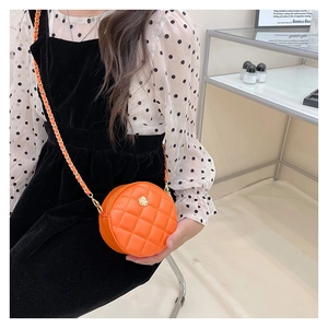 Detail of orange quilted mini round bag featuring gold flower clasp and chain strap