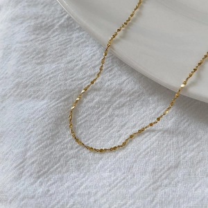 Detailed view of a gold stainless steel chain necklace on white fabric and ceramic