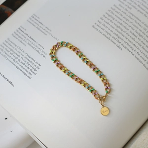 Detail of gold chain bracelet with colorful enamel links and Lucky coin on art book