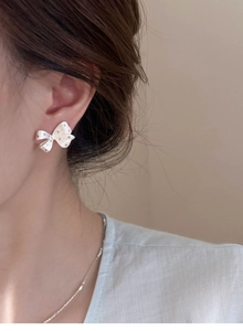 Close-up of silver bow stud earrings with dotted texture worn by a model in natural light