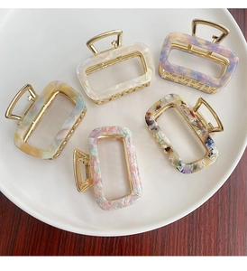 Collection of acetate rectangular hair claws in various marble colors on ceramic tray