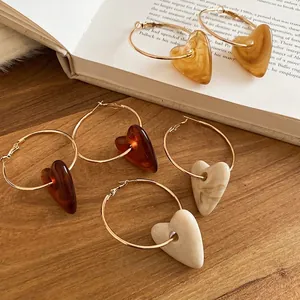 Hoop earrings with acrylic heart pendants in amber and marble finish on wooden desk
