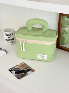 Detail of light green nylon toiletry bag with padded handle and woven label on white shelf