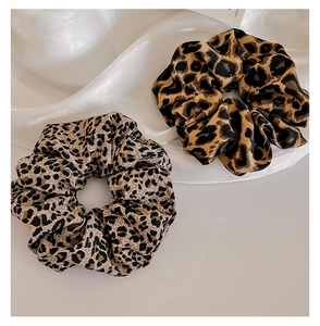 Detail of leopard print scrunchies in light and dark patterns on a white satin surface