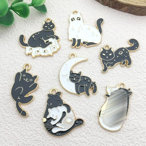 Flat lay of seven black and white enamel cat charms with gold moon and star accents