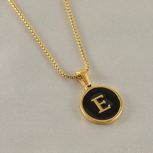 Gros plan du collier doré avec pendentif lettre E et émail noir sur breloque ronde