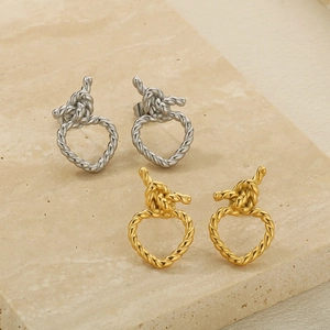 Détail de boucles d'oreilles cœur tressées en or et argent sur support en pierre