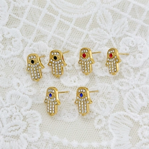 Detailed close-up of gold Hamsa Hand earrings with zircon inlays on lace background
