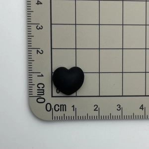 Detail shot showing a 1.2cm black heart resin charm next to a ruler for scale reference