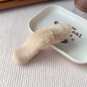 Detail view of plush beige faux fur hair clip on a white decorative tray with soft shadows