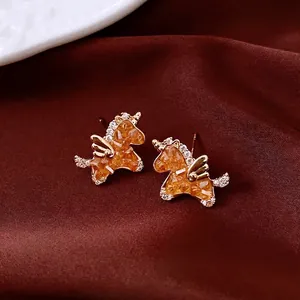 Golden unicorn stud earrings with amber crystal and white diamonds on red silk background