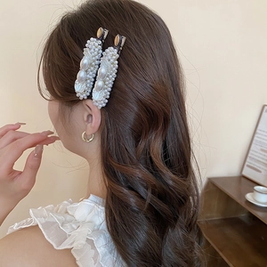 Detail of elegant pearl hair clips worn by a model in a warm, stylish setting