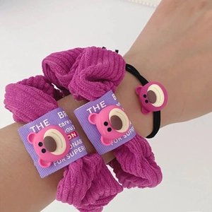 Detail of purple corduroy scrunchie and black hair tie with pink cartoon bear charm