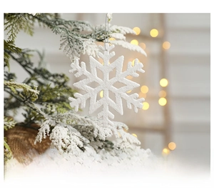 Close-up of white snowflake ornament with glitter on snowy pine branch with bokeh lights