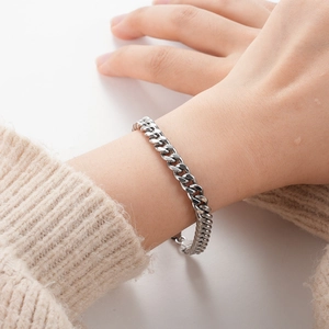 Detailed view of a silver stainless steel Cuban link bracelet worn on a model's wrist