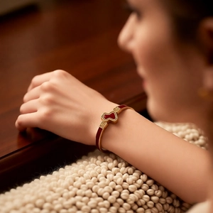 Close-up of 18k gold plated bangle featuring a red enamel gourd clasp with intricate etching