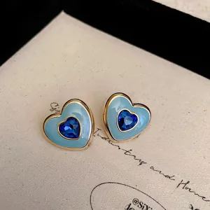Detailed close-up of French heart earrings with blue enamel and crystal inlay on beige card