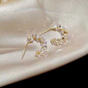 Close-up of golden C-shaped hoop earrings with shimmering zircons on champagne satin