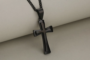 Macro detail of a layered black stainless steel cross pendant with high-gloss finish