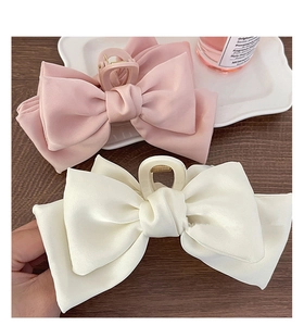 Detailed macro view of pink and cream satin oversized bow hair claws on a wooden table