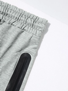 Dettaglio dei pantaloni sportivi grigi con elastico in vita e tasca con zip termosaldata
