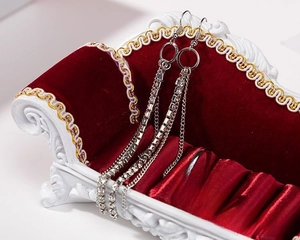 Detail of silver rings and rhinestone tassel earrings on a red velvet mini sofa stand