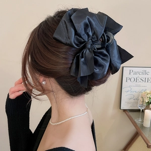 Detail of elegant black satin bow hair claw clip styled on woman's hair in a warm setting