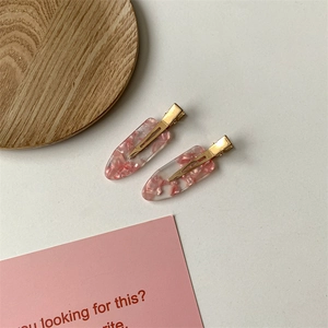 Detail view of two pink resin hair clips with golden duckbill clips on a minimalist background