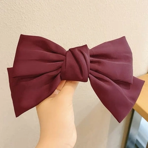 Detailed close-up of a large dark red satin ribbon bow hair clip held by hand