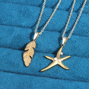 Detail of gold titanium steel leaf and starfish necklaces on blue velvet display