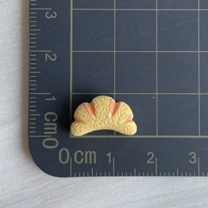 Miniature resin croissant charm shown on a centimeter ruler for size reference