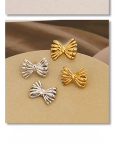 Gros plan de boucles d'oreilles nœuds dorées et argentées sur un support beige rond