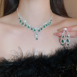 Detailed close-up of silver necklace and earrings set with green teardrop gems