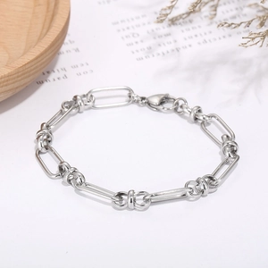 Detailed close-up of a silver knot chain bracelet with lobster clasp on a white table