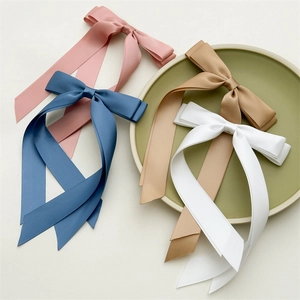 Close-up of four satin ribbon bow hair clips in pink, blue, beige, and white colors