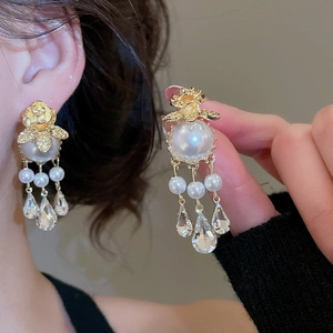 Close-up of golden flower bee earrings with pearl tassels and water-drop crystals