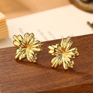 Close-up of golden flower stud earrings with intricate petal textures on dark wood