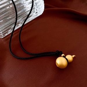 Macro detail of matte gold gourd pendant on black cord over red silk background