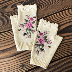 Close-up of beige knitted fingerless gloves featuring rose and bee floral embroidery
